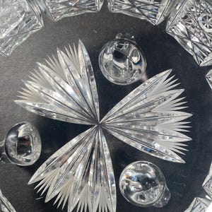 May include: A clear glass bowl with a cut glass design. The bowl has three feet and is sitting on a black surface.