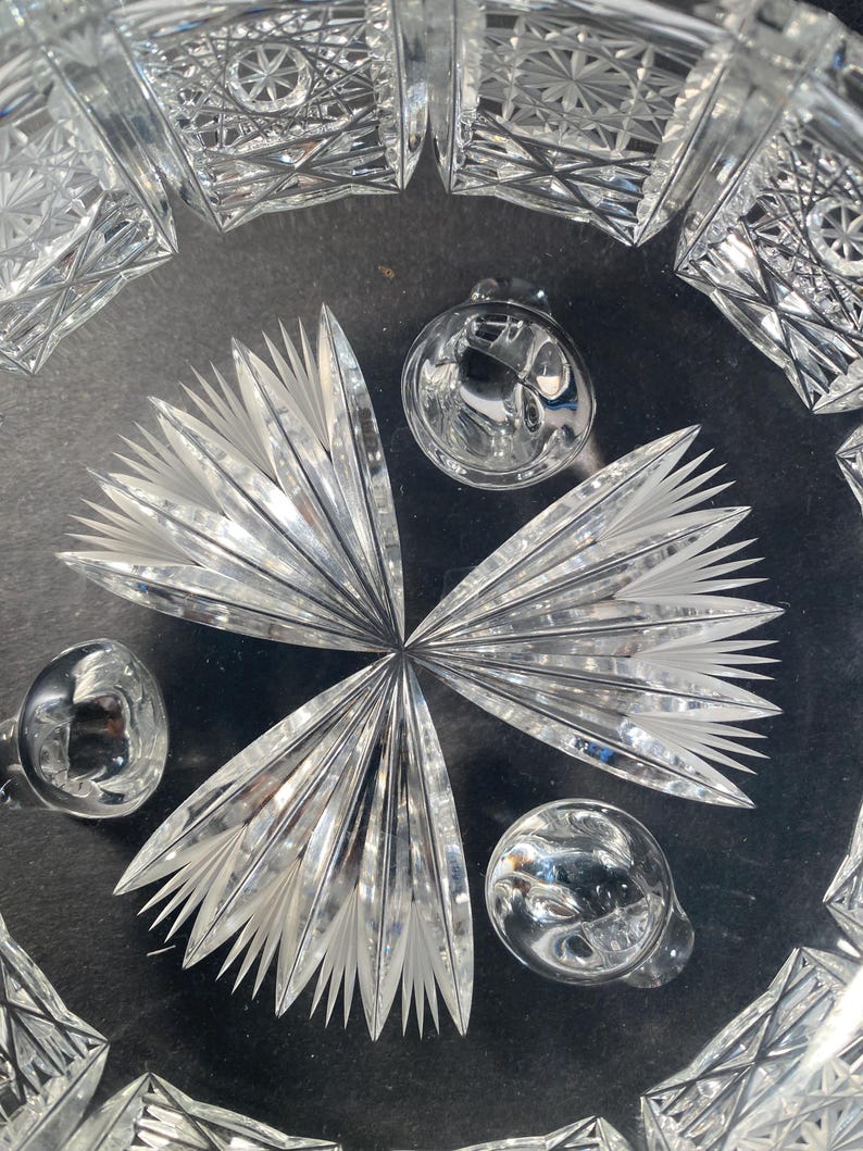 May include: A clear glass bowl with a cut glass design. The bowl has three feet and is sitting on a black surface.