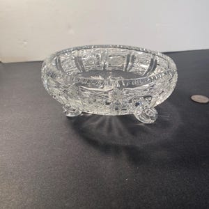May include: A clear glass bowl with a cut glass design and three legs. The bowl is on a black surface.