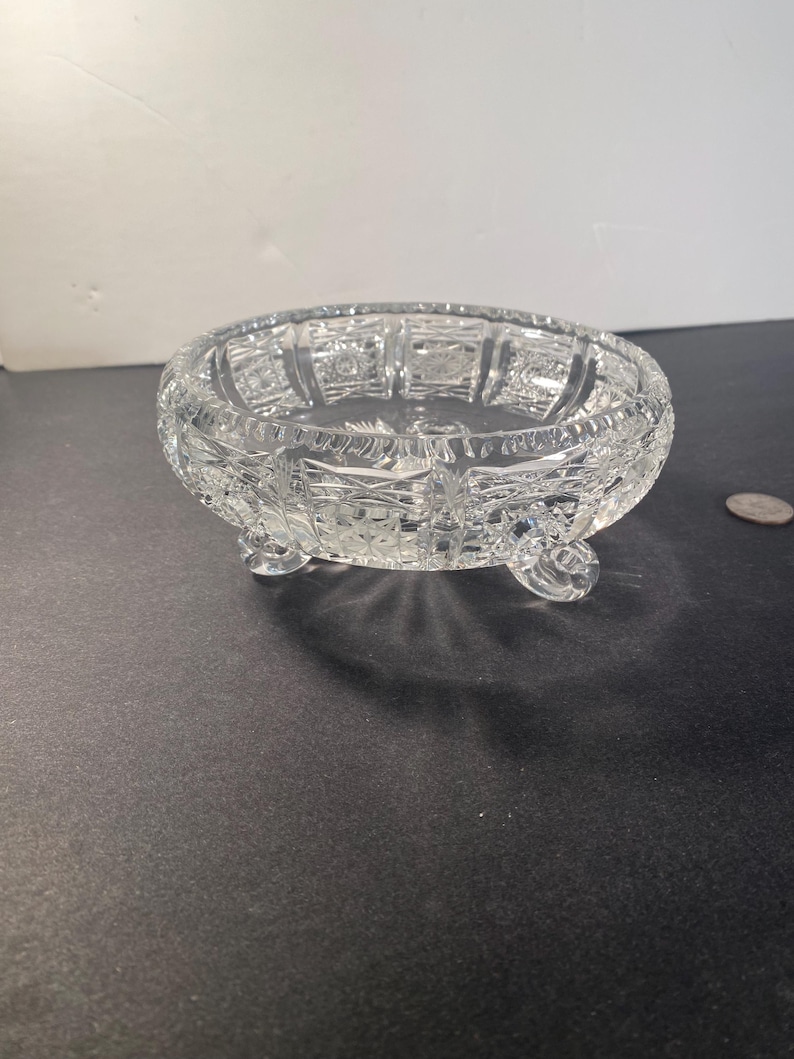 May include: A clear glass bowl with a cut glass design and three legs. The bowl is on a black surface.