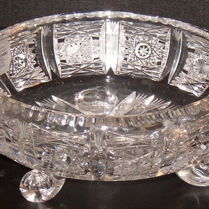 May include: A clear glass bowl with intricate cut designs and three feet. The bowl has a label that reads "Swarovski" and "Made in Austria".