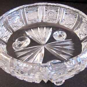 May include: A clear glass bowl with intricate cut designs and three feet. The bowl has a starburst pattern in the centre and a geometric pattern around the rim.