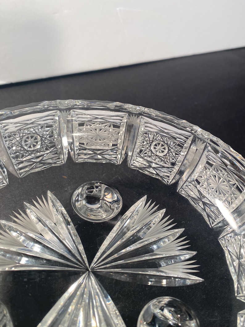 May include: A clear glass bowl with a cut glass design. The bowl has a scalloped edge and a starburst pattern in the centre.
