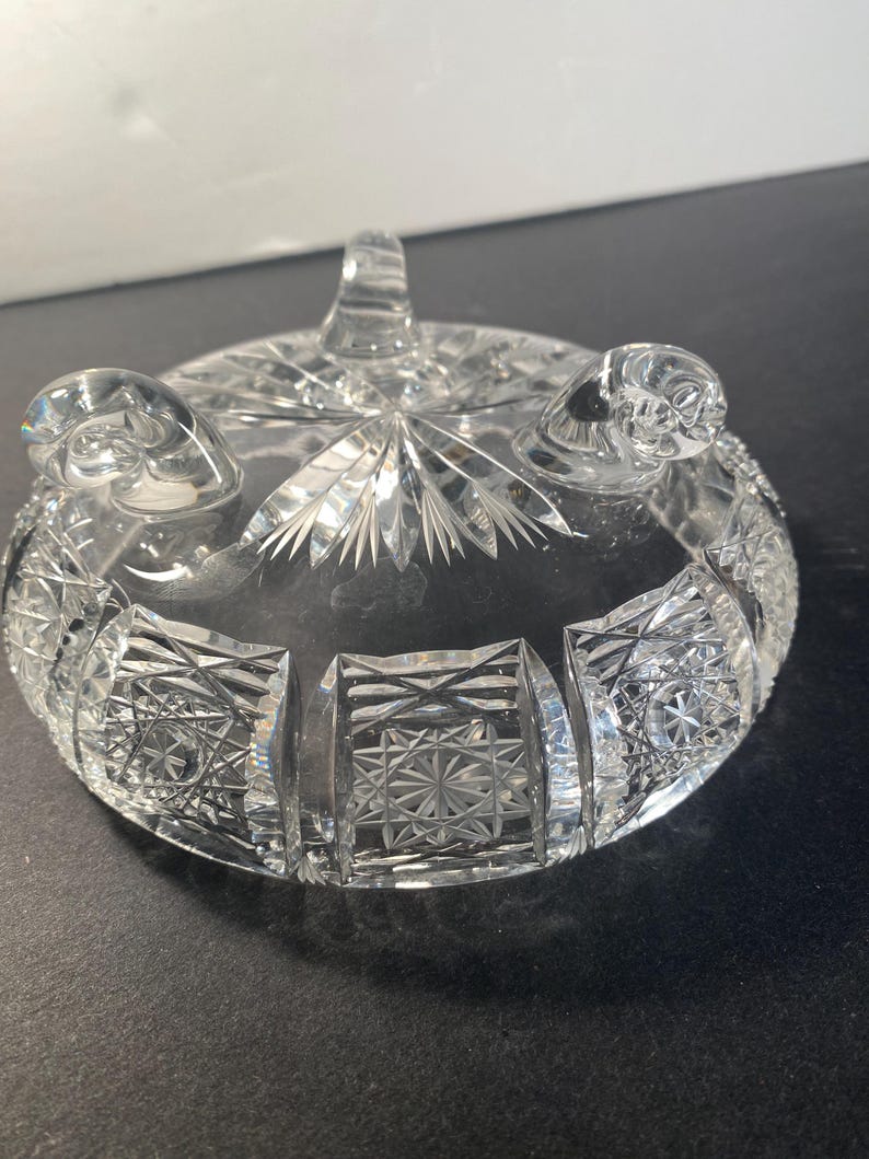 May include: A clear glass bowl with a cut glass design. The bowl has three feet and is ideal for serving snacks or desserts.
