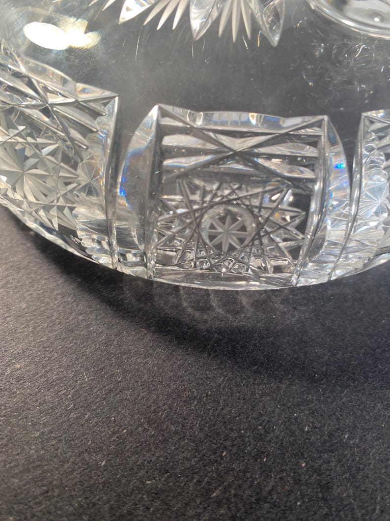 May include: A clear glass bowl with a cut glass design. The bowl has a starburst pattern in the centre and a geometric pattern around the rim.