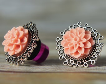 May include: A pair of silver and peach flower ear gauges. The gauges feature a delicate silver filigree design with a peach-colored flower in the center.