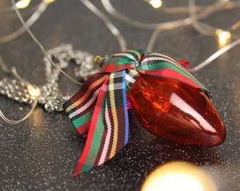 May include: A red glass lightbulb ornament with a plaid ribbon tied around it. The ornament is hanging from a silver chain.