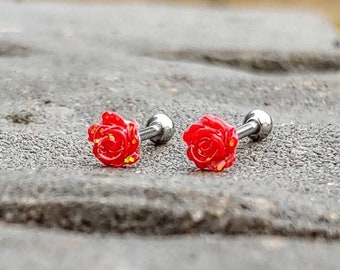 May include: Two red rose flower earrings with silver posts. The earrings are on a gray surface.
