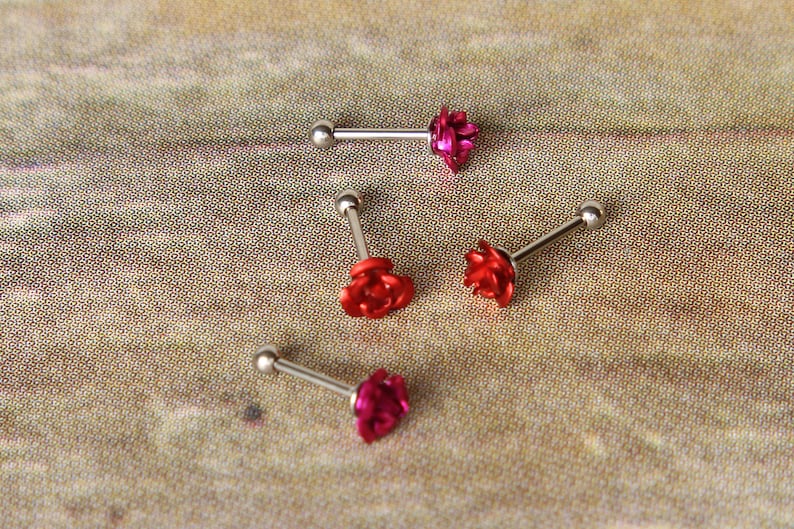 May include: Four pieces of body jewelry with a floral design. Each piece has a silver-colored barbell with a small, round ball on one end and a flower on the other. The flowers are red and pink.