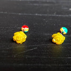 May include: A pair of yellow rose flower earrings with a red, green, and blue ball on the top of each earring.