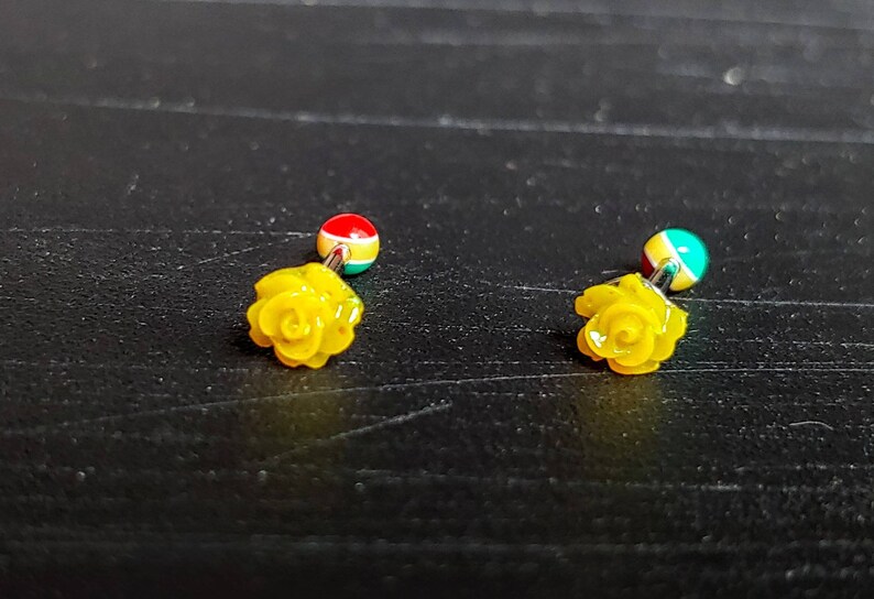 May include: A pair of yellow rose flower earrings with a red, green, and blue ball on the top of each earring.