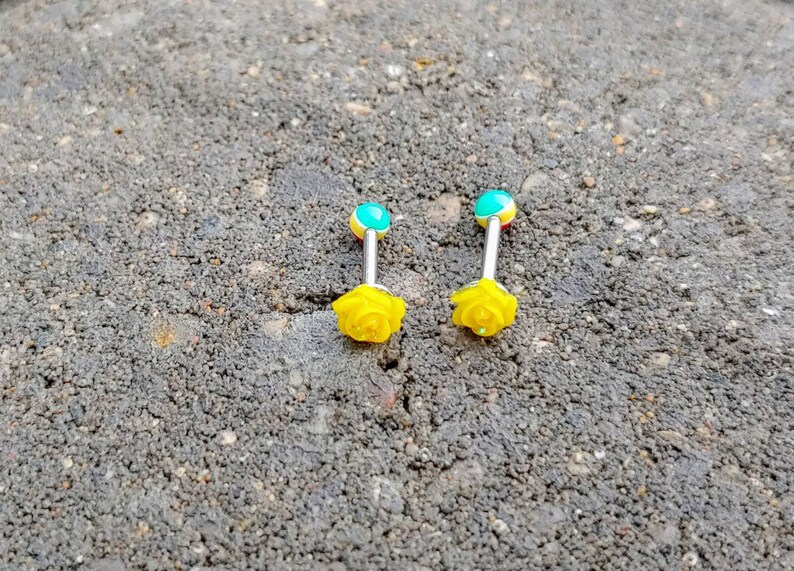 May include: Two yellow rose flower barbell tongue rings with turquoise and yellow accents.
