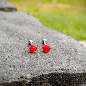 May include: Two silver barbell earrings with red rose accents. The roses are detailed with yellow centers.