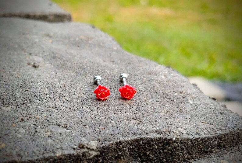 May include: Two silver barbell earrings with red rose accents. The roses are detailed with yellow centers.