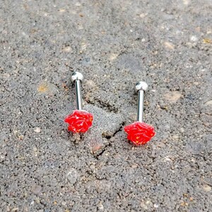 May include: Two silver barbell tongue rings with red rose-shaped charms.