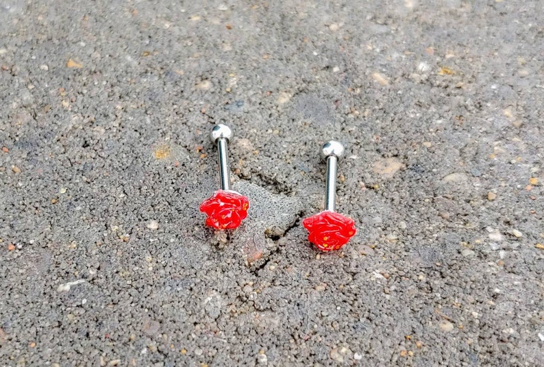 May include: Two silver barbell tongue rings with red rose-shaped charms.