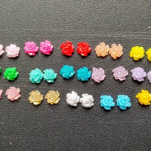 May include: Assortment of 20 colorful plastic rose flower embellishments. The roses are in various colors, including pink, red, blue, green, yellow, and white.