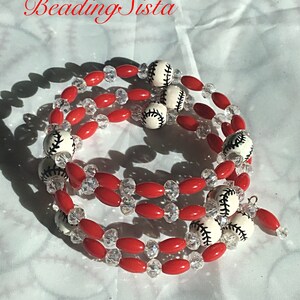 May include: A triple-strand bracelet with red and clear beads, and white baseball-shaped beads with black stitching.