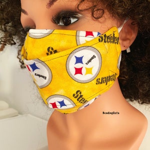 May include: A yellow face mask with the Pittsburgh Steelers logo repeated on the fabric. The mask has a white elastic band on each side.