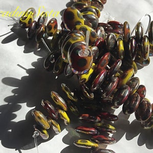 May include: A strand of oval-shaped glass beads with a yellow and red iridescent finish. The beads have a polka dot pattern and are strung on a clear thread.