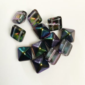 May include: A group of 10 iridescent black and purple square beads with a pyramid shape. The beads have a silver stripe across the center.