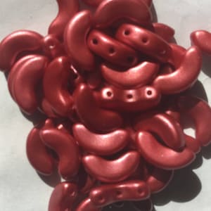 May include: A pile of small, crescent-shaped beads in a metallic rose gold color. The beads have a smooth, shiny finish and are perfect for jewelry making.