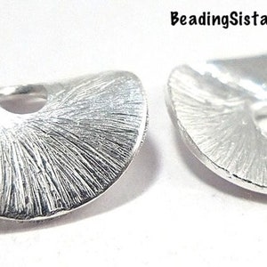 May include: Two silver metal bead caps with a textured finish and a round hole in the center. The caps are shaped like a half-circle.