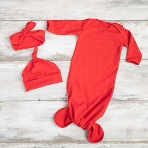 以下が含まれることがあります： 赤い長袖のベビーガウンと、結び目の付いた足。それに合わせて、赤いヘッドバンドと帽子もセットになっています。