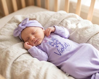 Geborduurde babyjurk met violetgeknoopte naam en hoge hoed of hoofdband