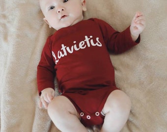 Burgundy baby bodysuit with white text "Latvietis" or "Latviete"