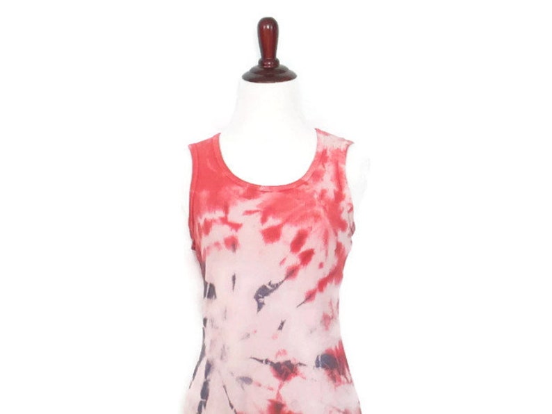 May include: A sleeveless tie-dye tank top in shades of red, pink, and white. The top has a relaxed fit and a scoop neck.