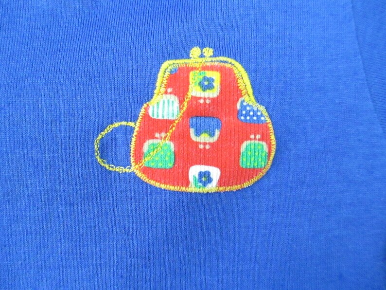 May include: A red, blue, and green patchwork purse with a gold chain, embroidered on a blue fabric.