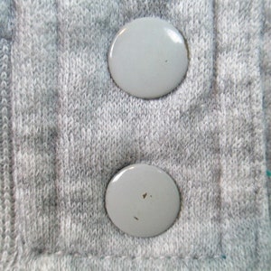 May include: Close-up of two gray plastic buttons on a gray knitted fabric.