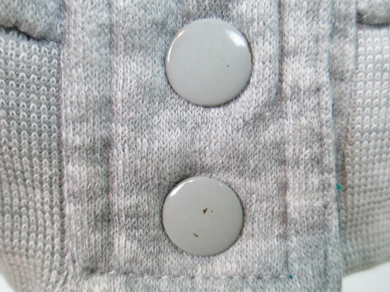 May include: Close-up of two gray plastic buttons on a gray knitted fabric.