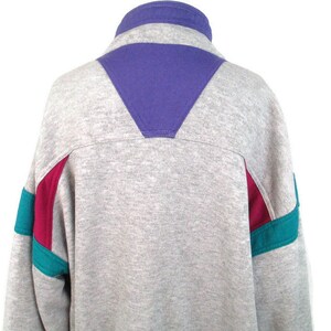 May include: A gray sweatshirt with a purple, teal, and burgundy color block design. The sweatshirt has a high collar and a zipper.