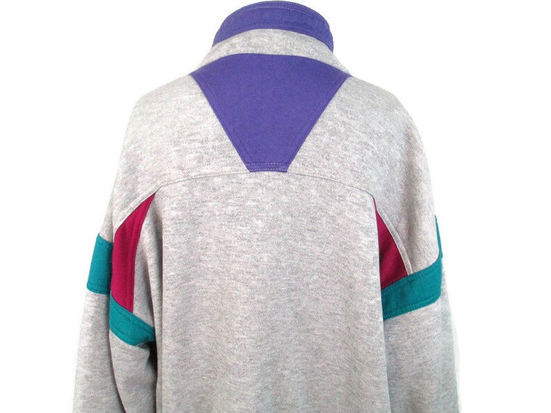May include: A gray sweatshirt with a purple, teal, and burgundy color block design. The sweatshirt has a high collar and a zipper.