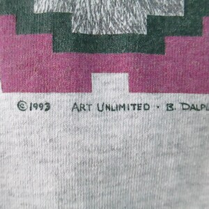 Op de afbeelding: Een grijs T-shirt met een geometrisch ontwerp in roze, groen en grijs. De tekst "&copy; 1993 ART UNLIMITED - B. DALPIAZ" staat onderaan het shirt gedrukt.