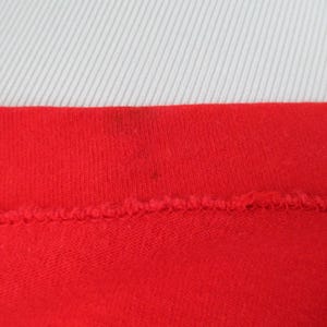 Pu&ograve; includere: Primo piano della cucitura rossa di un capo di abbigliamento. Il tessuto &egrave; a maglia e ha una texture liscia.