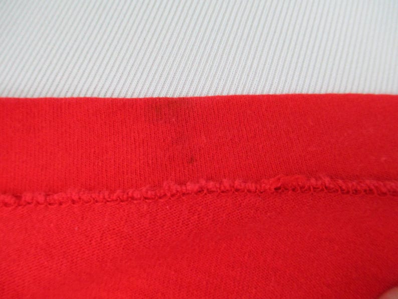 Pu&ograve; includere: Primo piano della cucitura rossa di un capo di abbigliamento. Il tessuto &egrave; a maglia e ha una texture liscia.
