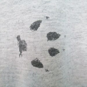 Op de afbeelding: Een close-up van een grijze stof met een zwart splatterpatroon.