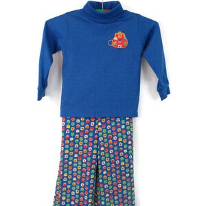May include: A blue turtleneck shirt with a red purse embroidered on the front, paired with blue pants with a colorful polka dot pattern.