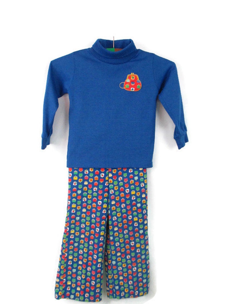 May include: A blue turtleneck shirt with a red purse embroidered on the front, paired with blue pants with a colorful polka dot pattern.