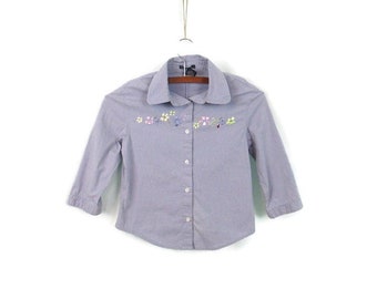 May include: A light blue and white striped button-down shirt with embroidered flowers in shades of pink, purple, and green.