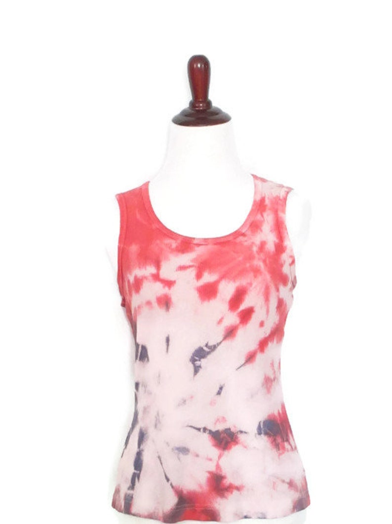 May include: A sleeveless tie-dye tank top in shades of red, pink, and white. The top has a scoop neck and a relaxed fit.