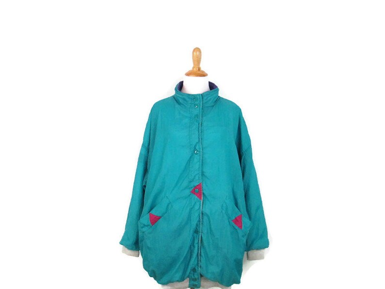 May include: A teal blue jacket with a zipper closure and pink accents. The jacket has a stand-up collar and long sleeves.