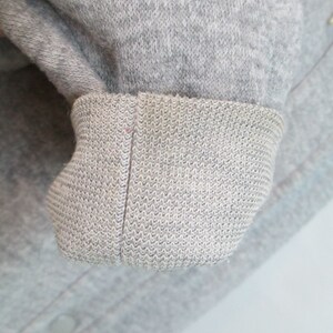 May include: Close-up of a gray sweatshirt cuff. The cuff is made of a soft, knitted fabric.