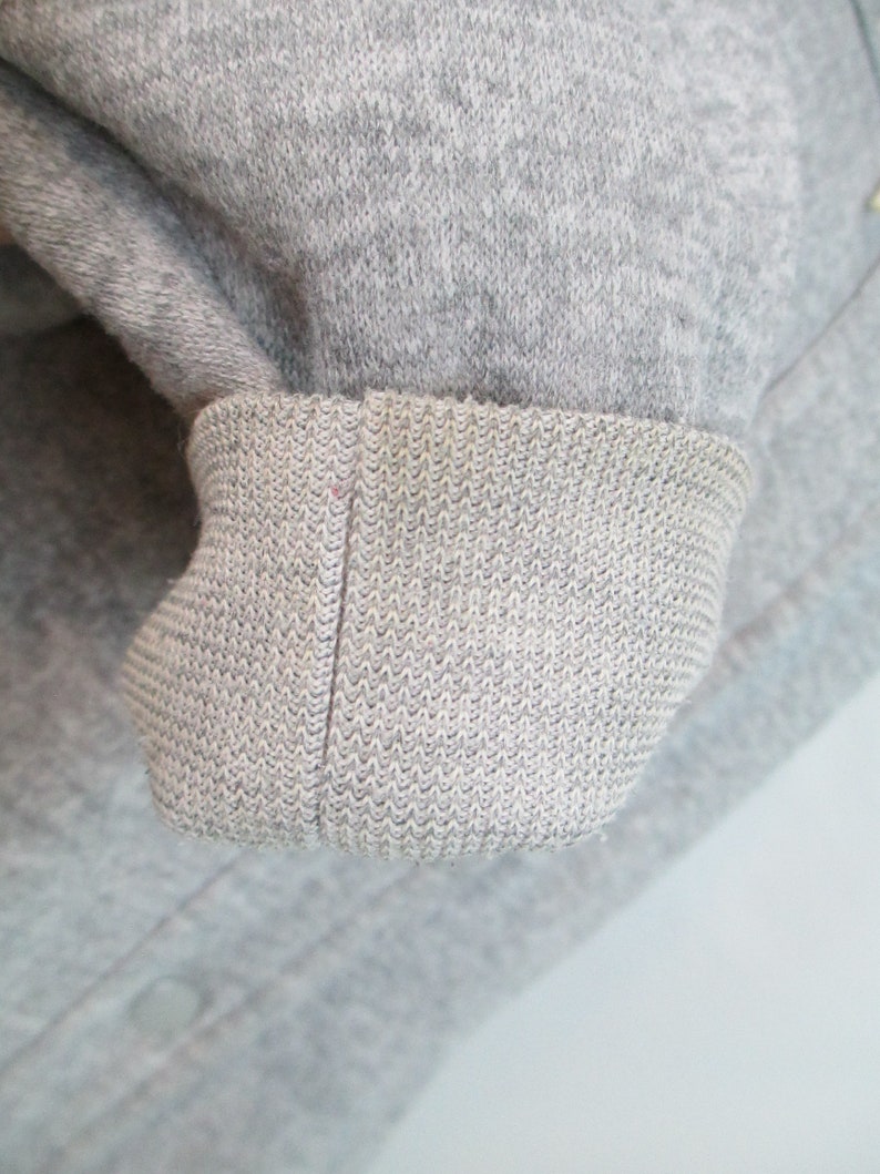May include: Close-up of a gray sweatshirt cuff. The cuff is made of a soft, knitted fabric.