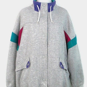 May include: A gray sweatshirt jacket with a snap closure and a high collar. The jacket has purple and teal colored stripes on the sleeves.