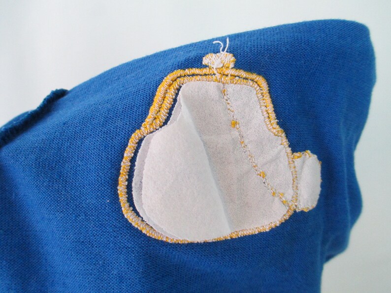 May include: A blue fabric patch with a yellow embroidered design of a purse. The purse is outlined in yellow and has a white fabric interior.