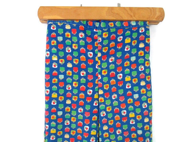 May include: Blue corduroy pants with a repeating pattern of small red, yellow, and green purses.